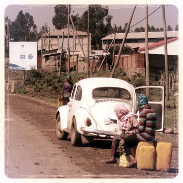 ladies taking a rest along their walk to get water (with our Volkswagon's cousin in the background, and a sign advertising clean water)